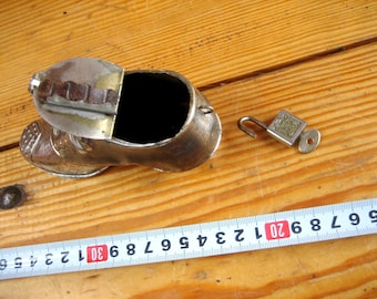 May include: A silver metal shoe-shaped trinket box with a hinged lid and a small lock and key. The box is sitting on a wooden surface with a measuring tape.