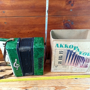 May include: A green accordion with a black and white keyboard and a white treble clef on the front. The accordion is in a cardboard box with the text "AKKOPAEOH" printed on the front.