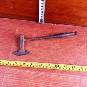 May include: A rusty metal tool with a curved blade and a wooden handle. The tool is about 20 inches long and is lying on a wooden surface.