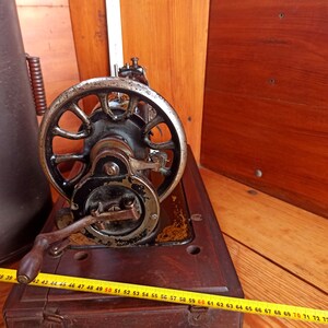 May include: A vintage sewing machine with a black metal body and a large, round, silver-colored wheel. The machine is sitting on a wooden table.