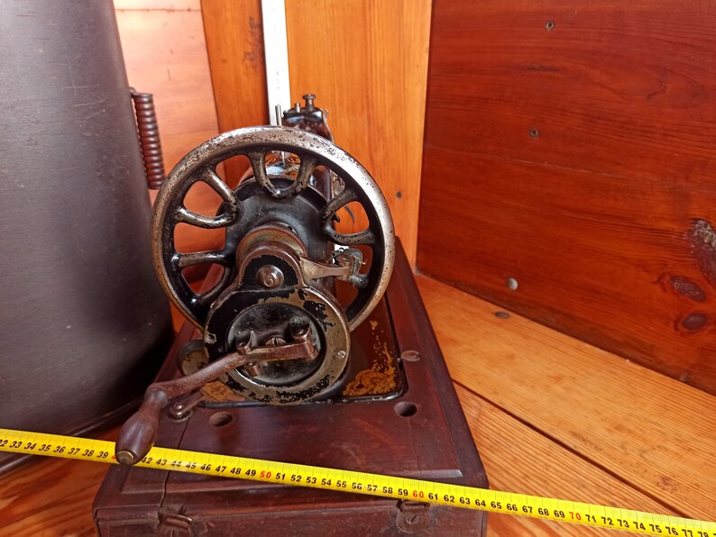 May include: A vintage sewing machine with a black metal body and a large, round, silver-colored wheel. The machine is sitting on a wooden table.