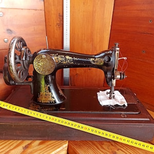 May include: A vintage black sewing machine with a wooden base and a yellow measuring tape. The machine has a decorative gold plate and a red thread.