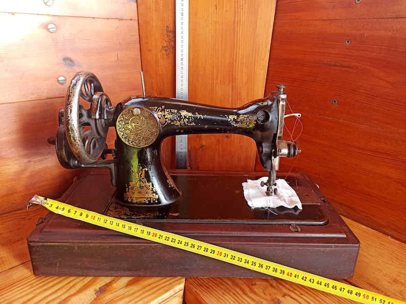 May include: A vintage black sewing machine with a wooden base and a yellow measuring tape. The machine has a decorative gold plate and a red thread.