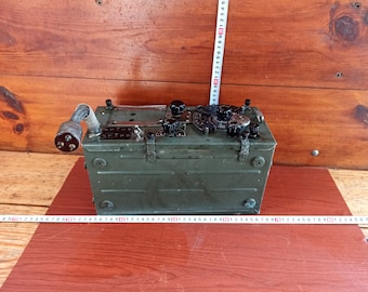 May include: A green metal box with a black antenna and several knobs and dials. The box has a black handle on the top and a black cord coming out of the side.