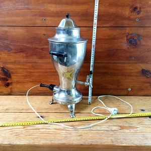 May include: A silver electric coffee pot with a black handle and a cord. The pot is sitting on a wooden surface.