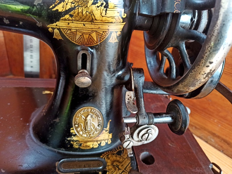 May include: A vintage black Singer sewing machine with gold accents and a decorative eagle design. The machine has a wooden base and a metal foot pedal.