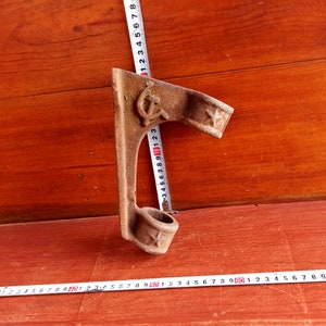 May include: A rusty metal hook with a hammer head and a ring at the top. The hook has a red star and hammer and sickle symbol on the side.