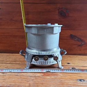 May include: A silver metal stove with three burners and a removable top. The stove is about 15 inches tall and has a decorative design.