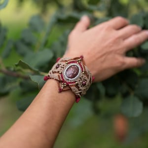 May include: A brown and red macrame bracelet with a large, oval-shaped, red gemstone in the center.