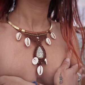 May include: A brown macrame necklace with a white stone pendant and white shell accents. The necklace is made with a gold chain and has a bohemian style.