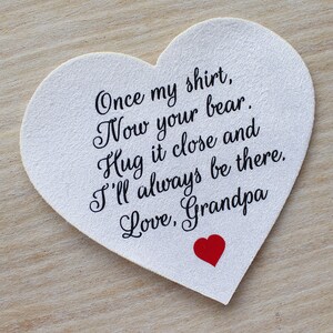 May include: A white heart-shaped card with the text "Once my shirt, Now your bear. Hug it close and I'll always be there. Love, Grandpa" in black script. A small red heart is at the bottom.