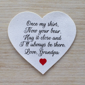 May include: White heart-shaped card with a handwritten message that reads "Once my shirt, Now your bear. Hug it close and I'll always be there. Love, Grandpa". A small red heart is drawn at the bottom of the card.