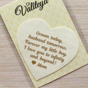 Peut inclure: Une carte en forme de cœur blanche avec une inscription dorée qui dit "Groom today, husband tomorrow. Forever my little boy. I love you to infinity and beyond! Mom."