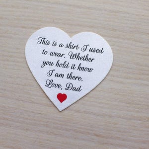 May include: A heart-shaped white felt keepsake with the text "This is a shirt I used to wear. Whether you hold it know I am there. Love, Dad" in black script. A small red heart is at the bottom.