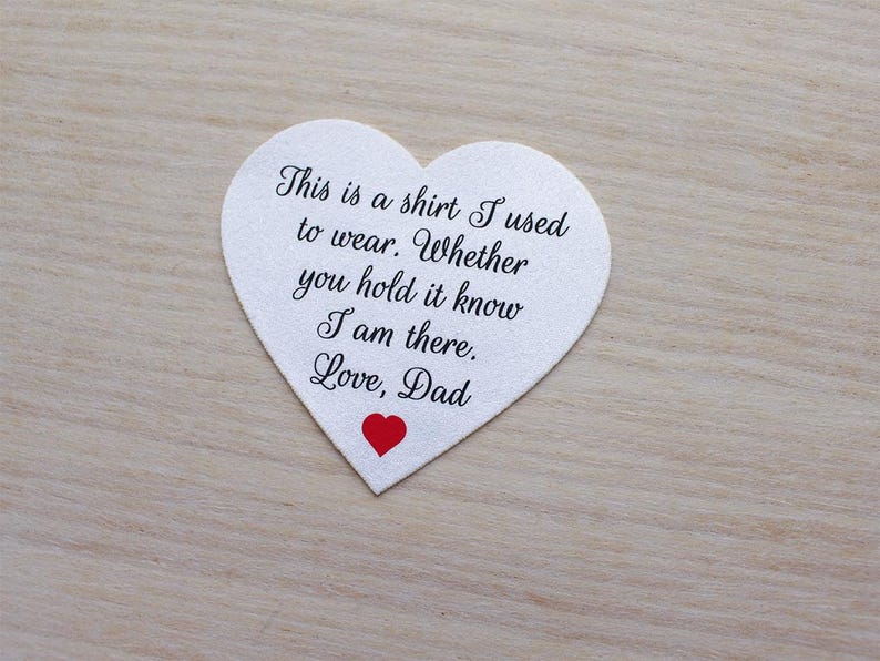 May include: A heart-shaped white felt keepsake with the text "This is a shirt I used to wear. Whether you hold it know I am there. Love, Dad" in black script. A small red heart is at the bottom.