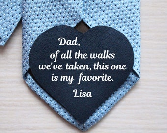 May include: A blue tie with a black heart-shaped tag attached to it. The tag has white text that reads "Dad, of all the walks we've taken, this one is my favorite. Lisa."
