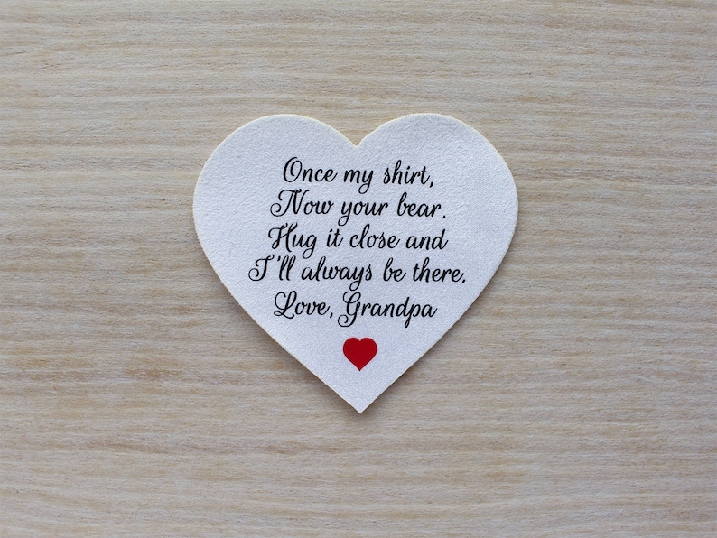 May include: A white heart-shaped keepsake with black script that reads "Once my shirt, Now your bear. Hug it close and I'll always be there. Love, Grandpa." A small red heart is at the bottom.
