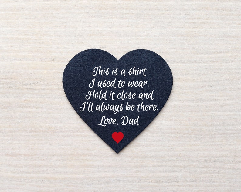 Może przedstawiać: Przedmiot w kształcie serca z ciemnoniebieskiej tkaniny z białym tekstem: "This is a shirt I used to wear. Hold it close and I'll always be there. Love, Dad." Na dole małe czerwone serce.