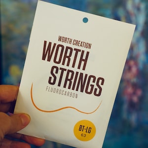 May include: A white package with the text "WORTH CREATION WORTH STRINGS FLUOROCARBON" and a yellow circle with the text "BT-LG 63".