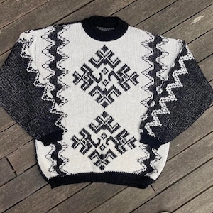 May include: A black and white knitted sweater with a geometric pattern. The sweater has a crew neck and long sleeves.