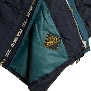 May include: A navy blue jacket with a teal lining and a zipper closure. The jacket has a label that reads "GORE-TEX Guaranteed to keep you dry".