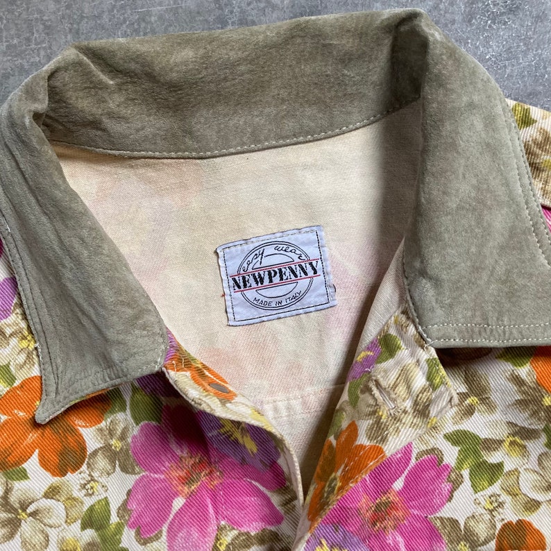 May include: A white button-up shirt with a floral print in shades of pink, orange, and green. The shirt has a green suede collar and a label that reads "Newpenny Made in Italy".