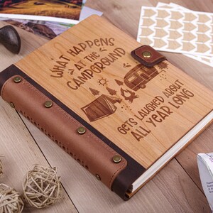 May include: A wooden journal with a brown leather cover and a quote about camping: "What happens at the campground gets laughed about all year long".