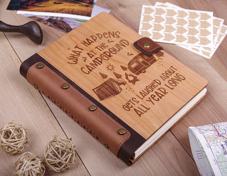 May include: A wooden journal with a brown leather cover and a quote about camping: "What happens at the campground gets laughed about all year long".