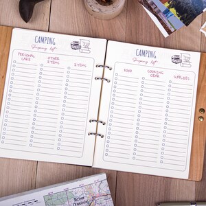 May include: A wooden-bound notebook with a white interior and a checklist for camping supplies. The notebook has a brown leather strap and is open to two pages with the headings "Personal Care", "Other Items", "Items", "Food", "Cooking Gear", and "Supplies".