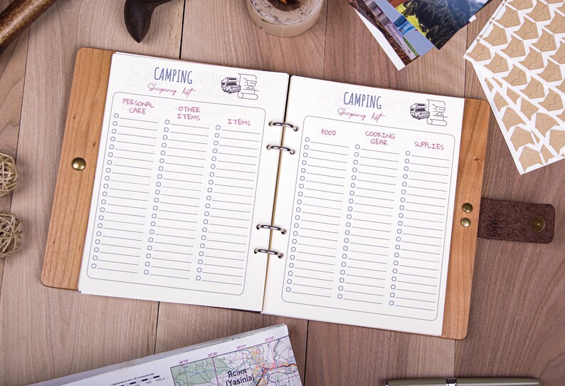 May include: A wooden-bound notebook with a white interior and a checklist for camping supplies. The notebook has a brown leather strap and is open to two pages with the headings "Personal Care", "Other Items", "Items", "Food", "Cooking Gear", and "Supplies".