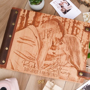 May include: A wooden photo album with a brown leather cover and a laser engraved image of a couple. The album has the text "Rick & Brittany Our Greatest Adventures" engraved on the front.