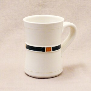 May include: White ceramic mug with a black and orange geometric design around the middle.