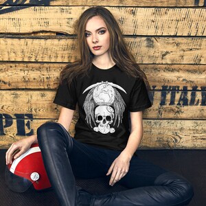 May include: A black t-shirt with a white graphic design of a skull with wings and a scythe. The graphic design also includes a globe and other small details.