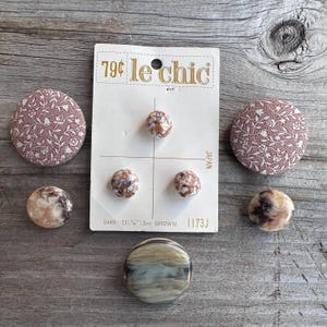 May include: A collection of vintage buttons and fabric-covered buttons in various sizes and designs. The card reads "79¢ le chic" and "JAPAN". The buttons include marbled, floral, and solid patterns. The card indicates the buttons are 21 mm (⅞") in diameter.