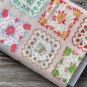 May include: A folded fabric with a repeating pattern of floral designs in pink, yellow, green, and blue. The fabric has a grid-like background in a light brown color. The floral designs are set against a white dotted background.