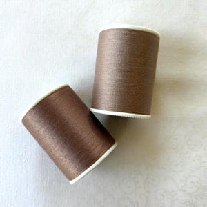 May include: A white ceramic mug with a black handle and the text "But First, Coffee" in a bold, black font. The mug is set against a blurred background, suggesting a cozy setting.