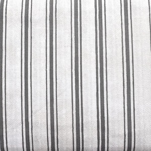 Può includere: Primo piano di un tessuto con un motivo a righe verticali. Il design presenta strisce alternate grigio chiaro e grigio scuro. Il tessuto ha un aspetto strutturato, che suggerisce una miscela di lino o cotone.