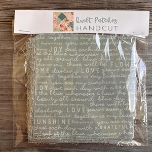 May include: A package of handcrafted quilt patches. The patches are a muted green color with white script text. The package has a white header with the text "Quilt Patches HANDCUT" and a floral design.