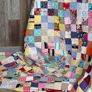 May include: A colorful patchwork quilt with a variety of fabric patterns and colors, including red, blue, yellow, and green. The quilt is made of numerous small squares sewn together, creating a textured surface. The quilt is folded over a surface.