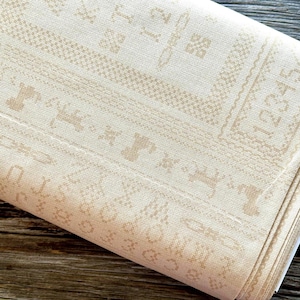 Puede incluir: Una taza de cerámica blanca con asa negra y el texto "But First, Coffee" en negrita negra. La taza se encuentra sobre un fondo borroso, sugiriendo un ambiente acogedor.