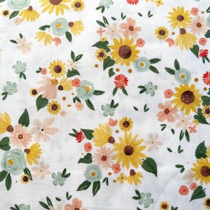May include: White fabric with a repeating floral pattern. The design features yellow sunflowers, peach and pink roses, and small blue and white flowers with green leaves. The flowers are scattered across the white background.