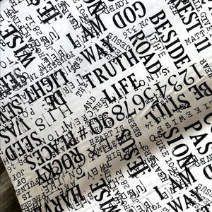 May include: White fabric featuring a black text design. The design includes words such as "Truth", "Life", and "God", alongside numbers and phrases from religious texts. The pattern repeats across the fabric.