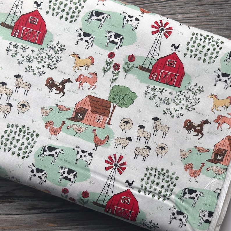 May include: White fabric with a repeating farm scene pattern. The design includes red barns, windmills, cows, horses, sheep, chickens, and flowers. The fabric has a light green and red color scheme.