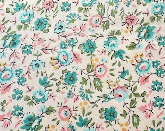 May include: Close-up of a fabric with a floral pattern. The design features small teal and pink flowers with green leaves on a cream-colored background. The flowers are arranged in a dense, repeating pattern.