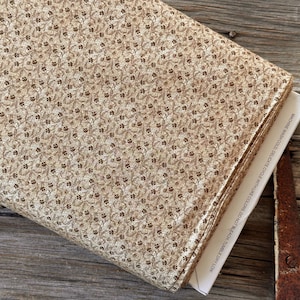 May include: A folded fabric roll with a repeating floral pattern in shades of tan and brown. The fabric is printed with small, stylized flowers and leaves. The edge of the fabric roll reveals a white label with care instructions.