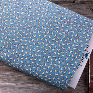 May include: A folded piece of blue fabric with a repeating pattern of small, abstract figures in cream and red. The fabric is resting on a wooden surface, with a white paper partially visible. The paper has the text "pixelable" and a blue bird logo.