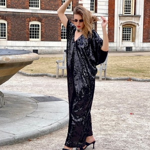 A white Italian actress wearing a party black sequin free size boubou jumpsuit with pockets and a detachable belt and posing by a fountain