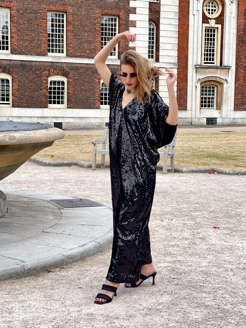 A white Italian actress wearing a party black sequin free size boubou jumpsuit with pockets and a detachable belt and posing by a fountain