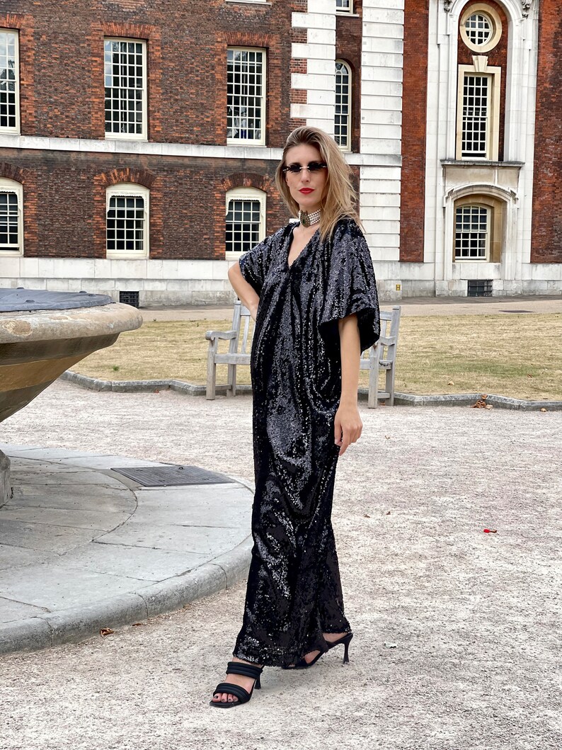A white Italian actress wearing a party black sequin free size boubou jumpsuit with pockets and a detachable belt and posing by a fountain