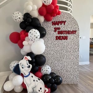 Könnte beinhalten: Eine festliche Partydekoration mit Dalmatiner-Thema. Eine große Ballongirlande in Rot, Schwarz und Weiß, mit Pfotenabdruck-Ballons, umrahmt eine Kulisse mit dem Text "Happy 3rd Birthday Dean". Ein Dalmatiner-Ausschnitt befindet sich am Boden.